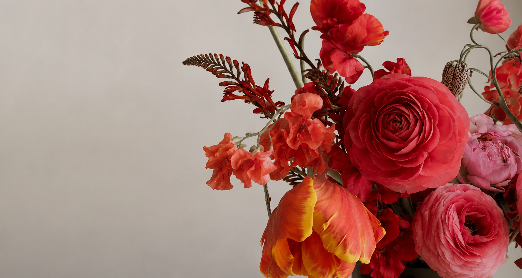 A hand-tied bouquet of red roses, orange ranunculus and pink peonies
